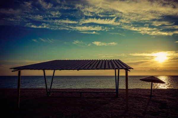 Навес и старый металлический зонтик на пустом песчаном пляже на закате . — стоковое фото