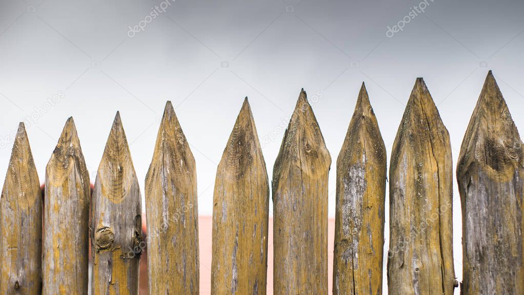 Fence made of sharp wooden stakes against the grey cloudy sky.