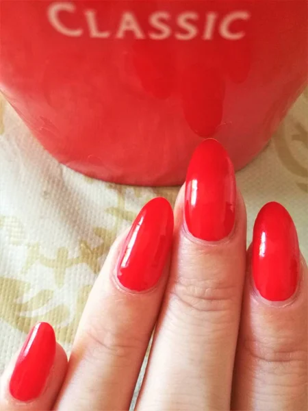 Closeup of Caucasian female hands with red manicure. Background text classic on a red mug