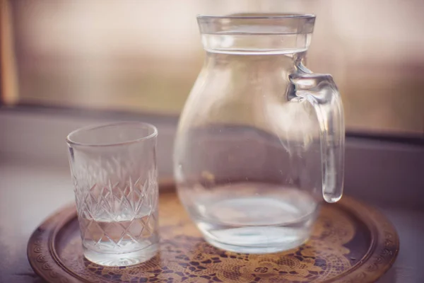 Jarra de agua y un vaso en una bandeja del alféizar de la ventana — Foto de Stock