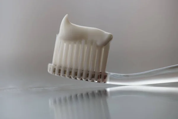 Escova de dentes de plástico transparente com pasta de dentes branca em uma mesa com reflexão sobre o vidro . — Fotografia de Stock