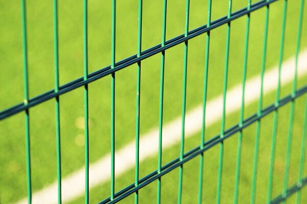 сетка зеленого забора на фоне газона для игры в мини-футбол
