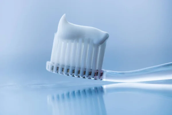 Escova de dentes de plástico transparente com pasta de dentes branca em um fundo branco azul com reflexão sobre o vidro . — Fotografia de Stock