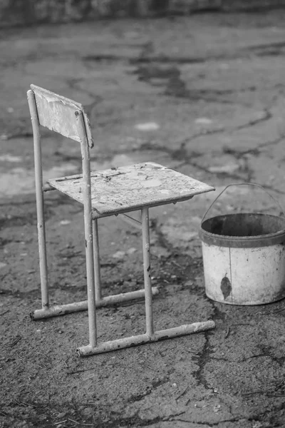 Cadeira velha e um balde estão no pátio rural. BW — Fotografia de Stock