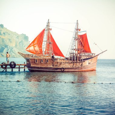 Deniz iskelede Dağları arka plan üzerinde kırmızı yelkenli bir gemi