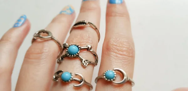 Bela mão feminina com muitos anéis diferentes. Manicure e design em unhas curtas na cor azul com um padrão floral . — Fotografia de Stock