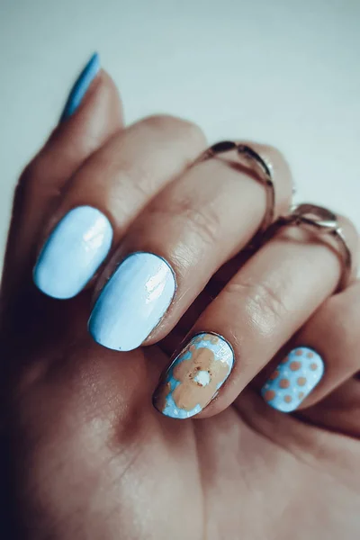 Bela mão feminina com anéis. Manicure e design em unhas curtas na cor azul com um padrão floral . — Fotografia de Stock