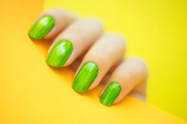 Ung kvinnas hand med vackra gröna manikyr innehar orange färg papper på gul bakgrund. — Stockfoto