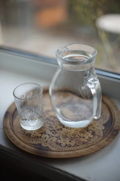 Jarra de agua y un vaso en una bandeja del alféizar de la ventana — Foto de Stock