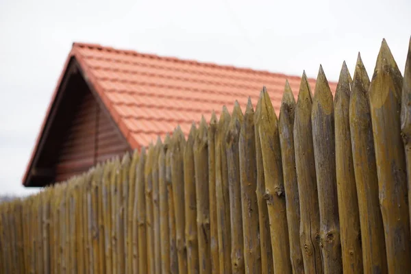 Ein Zaun aus scharfen Holzpfählen vor dem Hintergrund eines Holzhauses mit rotem Ziegeldach — Stockfoto