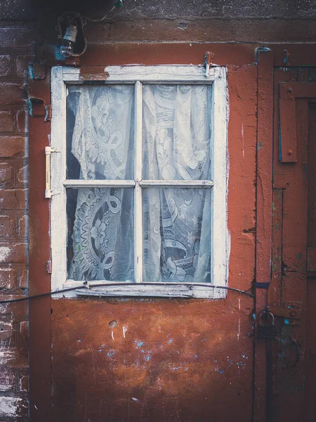 Fachada de um edifício velho, parede vermelha com janela branca e cortina — Fotografia de Stock