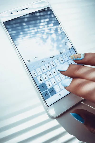 Mano femenina con clavos azules está escribiendo en un teléfono blanco un mensaje — Foto de Stock