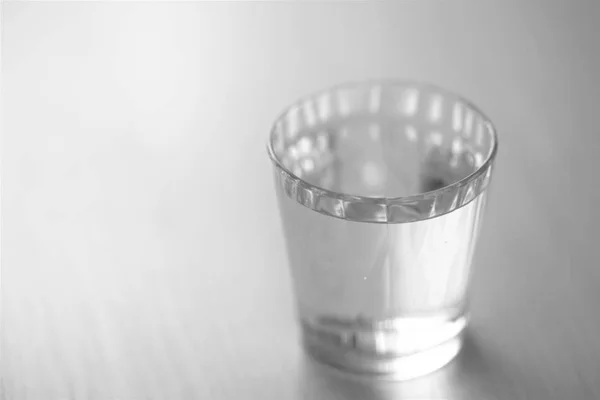 Glass full of water on the shiny table, selective art focus, BW — Stock Photo, Image