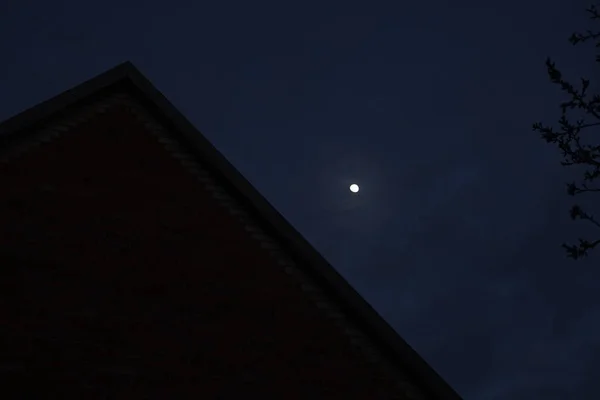 Ciemne nocne niebo z dużym księżycem nad dachem domu i gałęzi drzewa — Zdjęcie stockowe
