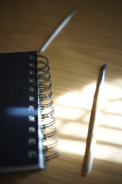 Caderno preto em uma espiral, escova e lápis em uma mesa com luz solar e sombras. Materiais para criatividade . — Fotografia de Stock