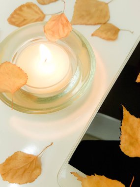 yanan mum, beyaz akıllı telefon ve sonbahar yaprakları.