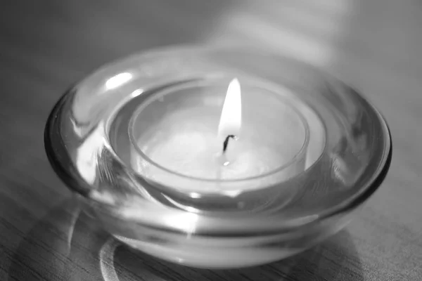 Low candle burns in a round glass candlestick, closeup, bw — Stock Photo, Image