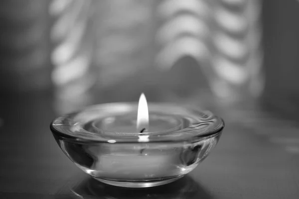 Candle burns in a round glass candlestick on the table, bw — Stock Photo, Image