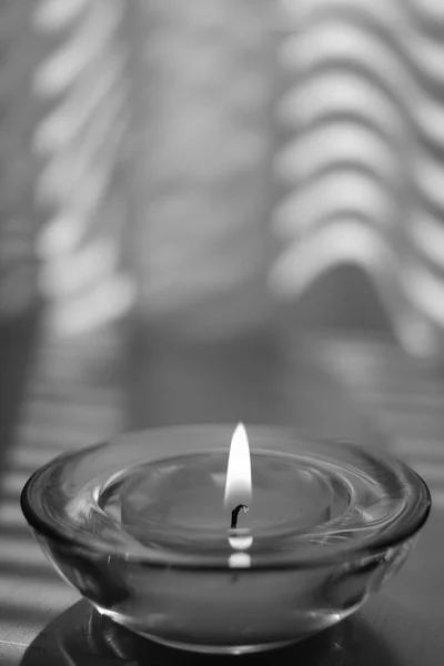 Small candle burns in a round glass candlestick on the table, bw photo — Stock Photo, Image