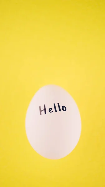 Uovo di pollo bianco con testo nero ciao su sfondo giallo . — Foto Stock