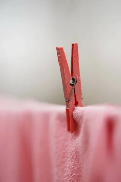 Pinza de ropa roja sostiene la ropa rosa en una cuerda, macro foto . — Foto de Stock