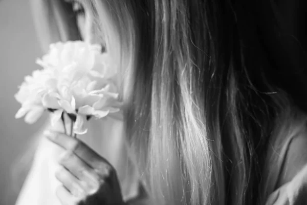 Blurred portrait of a young girl sniffing flowers in her hands, female dreams and pleasure. Black and white photo