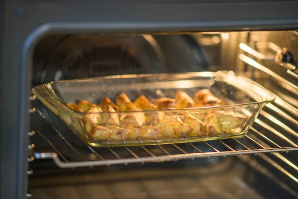 Готовые ломтики картофеля со специями лежат в стеклянной тарелке в духовке . — стоковое фото