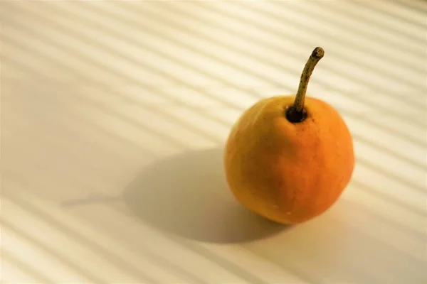 Fruta de pera madura naranja amarilla en un alféizar de ventana blanco con luz y tonos de las persianas — Foto de Stock