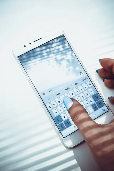 Mano femenina con clavos azules está escribiendo en un teléfono blanco un mensaje — Foto de Stock