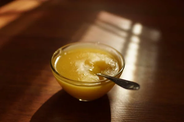 Runde Glasschale mit Honig und Löffel auf einem sonnigen Holztisch — Stockfoto