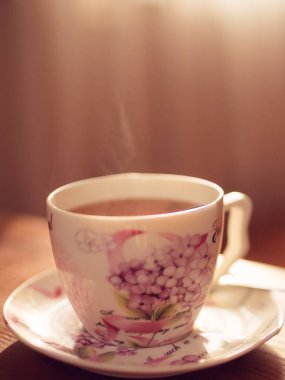 Zarif bir porselen fincanda siyah çay ve masanın üstünde buhar.