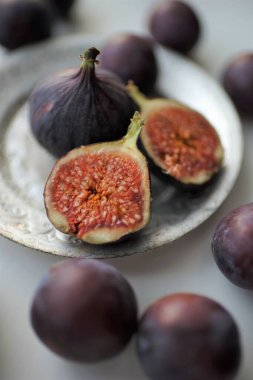 Olgun mor incirler, ortadan ikiye bölünmüş ve gümüş bir tabakla ve beyaz bir masanın üzerinde. Seçici sanat odağı.