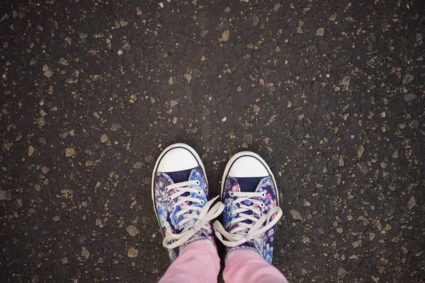 Damska stopa w niebieskich trampkach i różowe dżinsy na asfaltowej drodze, widok z góry — Zdjęcie stockowe