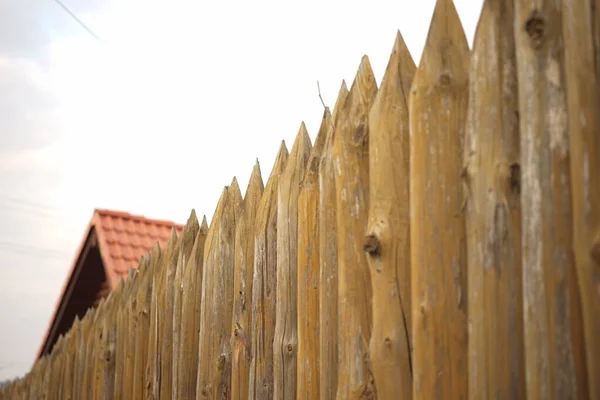 Ogrodzenie wykonane z ostrych drewnianych kołek i czerwonego dachówki pod błękitnym niebem — Zdjęcie stockowe