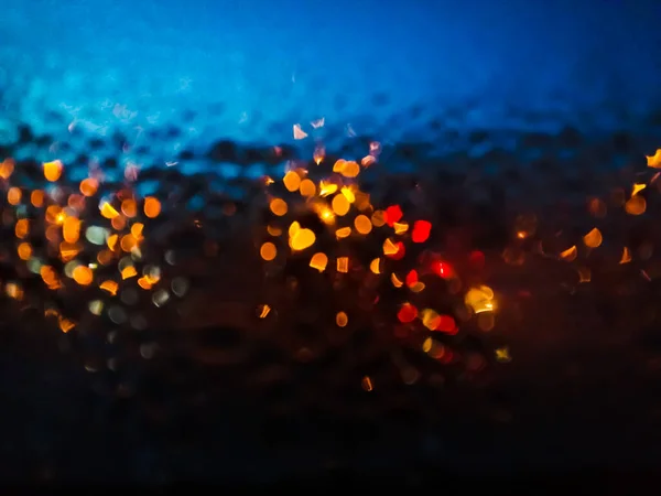 Night window with raindrops and street light of lanterns. Wet glass with multi-colored shiny drops. Blurred photo