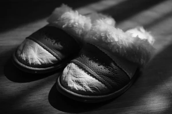 Women's slippers with a sheepskin on a wooden floor. BW photo. — Stock Photo, Image