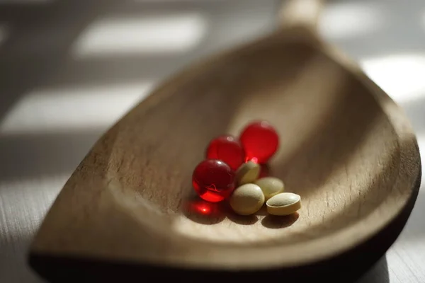 Sárga orvosi tabletták és vörös vitaminok egy fakanál. Gyógyszeres kezelés — Stock Fotó