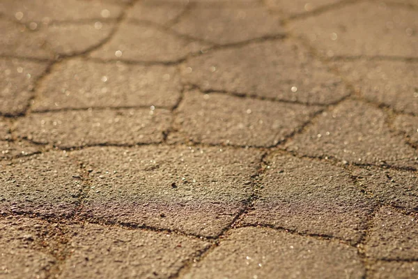 Çatlak, eski asfalttan yapılmış güneşli yol yüzeyi. Sıcak güneş ışığıyla taş dokusu — Stok fotoğraf