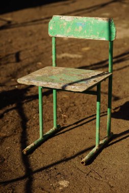 Bahçede, taş zeminde eski yeşil sandalye, sert ışık ve...