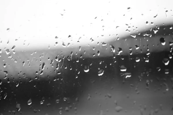 Janela molhada com gotas de chuva. Telhado e céu em fundo escovado. Tempo chuvoso . — Fotografia de Stock