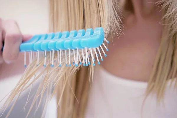 Young girl combing her wet blond hair with a blue comb, closeup — Stock Photo, Image