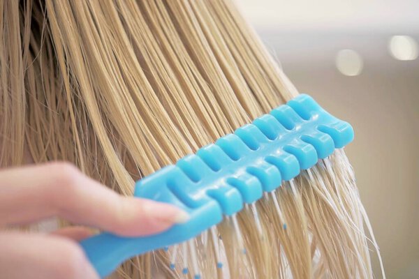 combing wet blonde hair with a blue comb, closeup