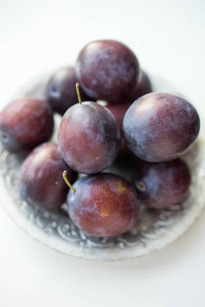 Ciruelas púrpuras maduras en un plato de plata sobre la mesa blanca — Foto de Stock