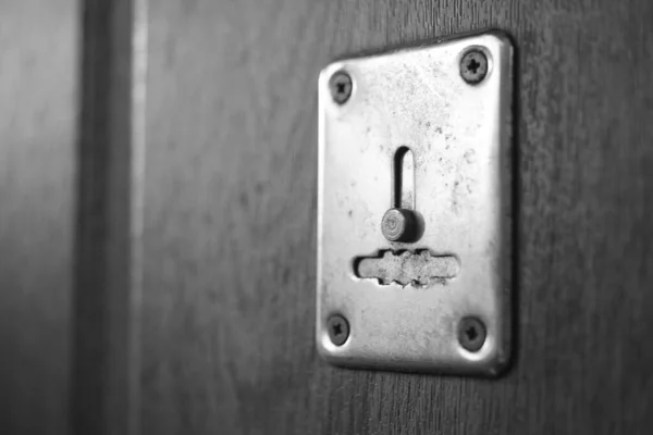 Houten deur met chromen sleutelgat en zonlicht, zwart-wit foto. — Stockfoto