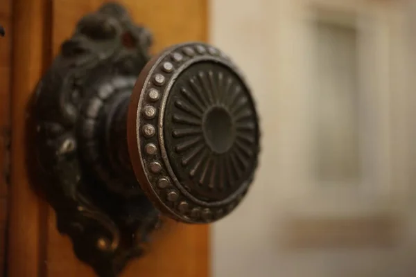 Punho de ferro redondo com um padrão em uma porta de madeira velha, close-up. Fundo em borrão de um edifício com uma janela . — Fotografia de Stock