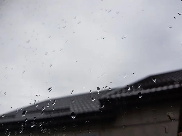 Okno zbliżeniowe z kroplami deszczu, zamglone zachmurzone niebo i dach domu w tle. — Zdjęcie stockowe