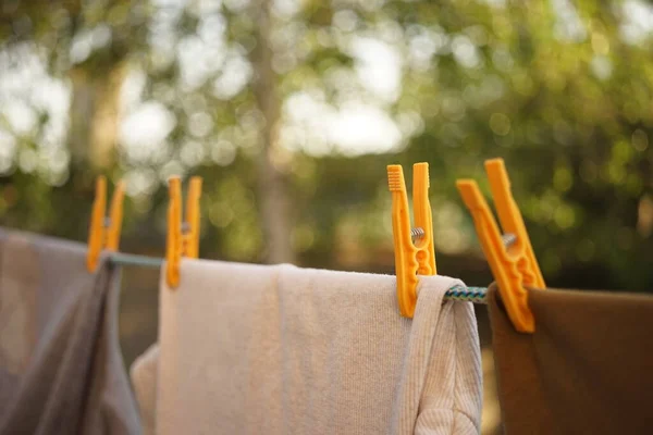 Diferentes ropas se secan en una cuerda con pinzas de ropa amarillas en un jardín de verano. Primer plano, fondo natural borroso . — Foto de Stock