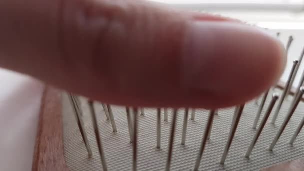 Les doigts femelles glissent sur les poils de fer d'une grande brosse à cheveux en bois. Macro vue de côté sur une table ensoleillée. — Video