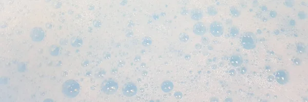 Espuma branca com bolhas que estouram na água azul, vista superior macro . — Fotografia de Stock