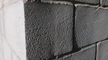 Büyük dikişli gri tuğladan yapılmış duvar. Beyaz plastik pencereli bir binanın ön cephesi, köşeden manzara